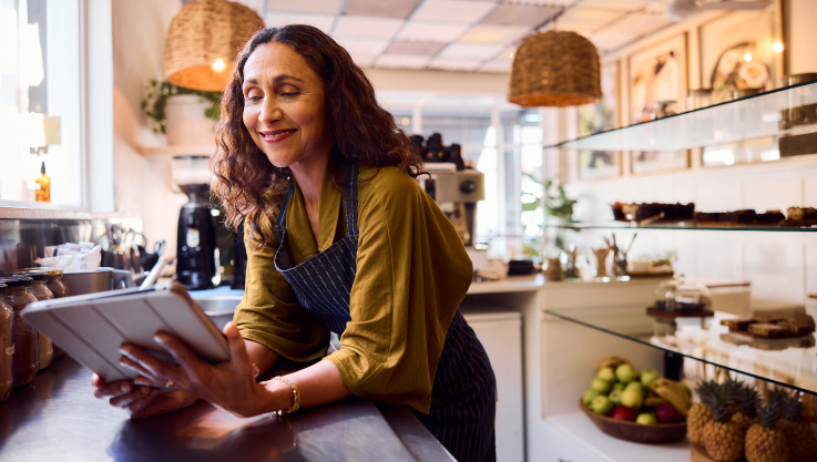 A woman leans against a counter in a store holding a tablet. 