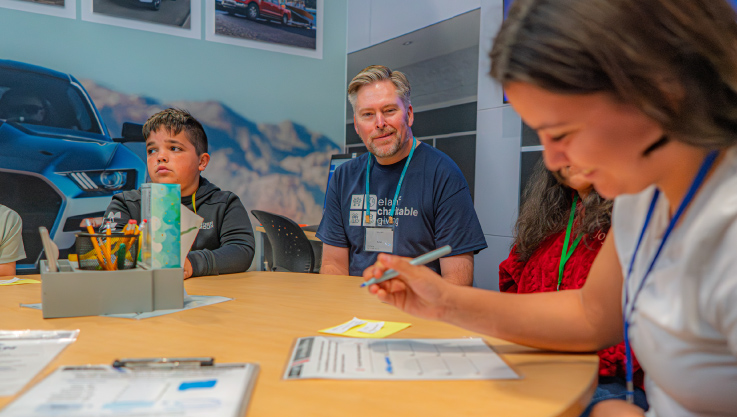 An adult volunteer sits at a table with children working.