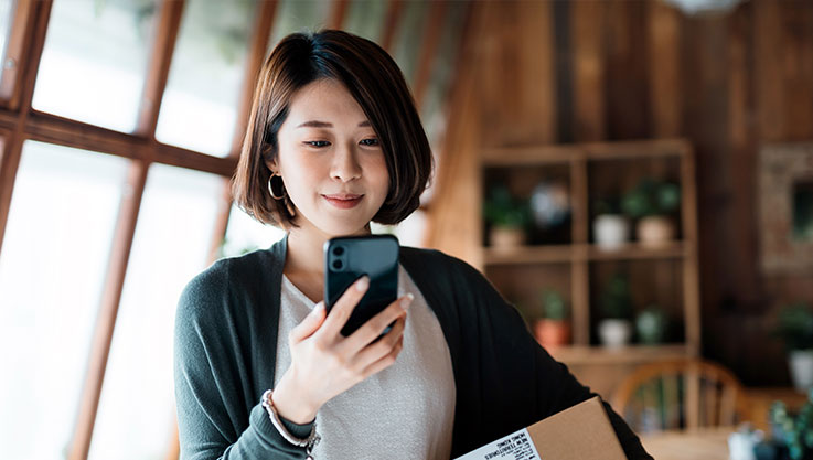 A woman stands in her home holding and looking at a cellphone.