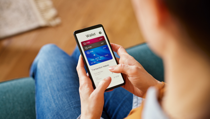 Over the shoulder of an adult you can see their mobile phone. On the screen is a digital wallet with multiple credit cards displayed.