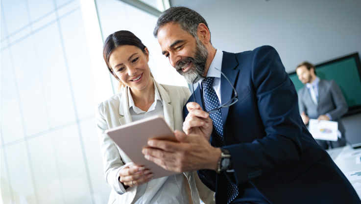 Two business people stand together looking at a tablet. 