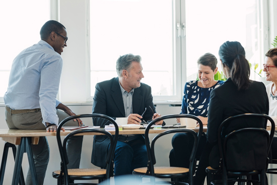 Team of 4 businesspeople sits at a table in conversation